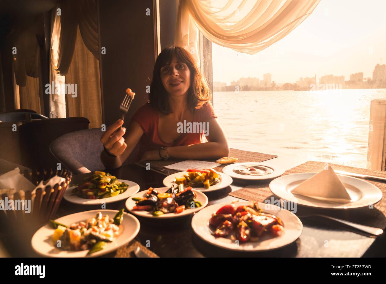 Ein junger Tourist mit Abendessen auf einem Boot auf dem nil ein traditionelles ägyptisches Essen mit Sonnenuntergang Licht im Fenster, die Stadt Kairo im Hintergrund. Stockfoto