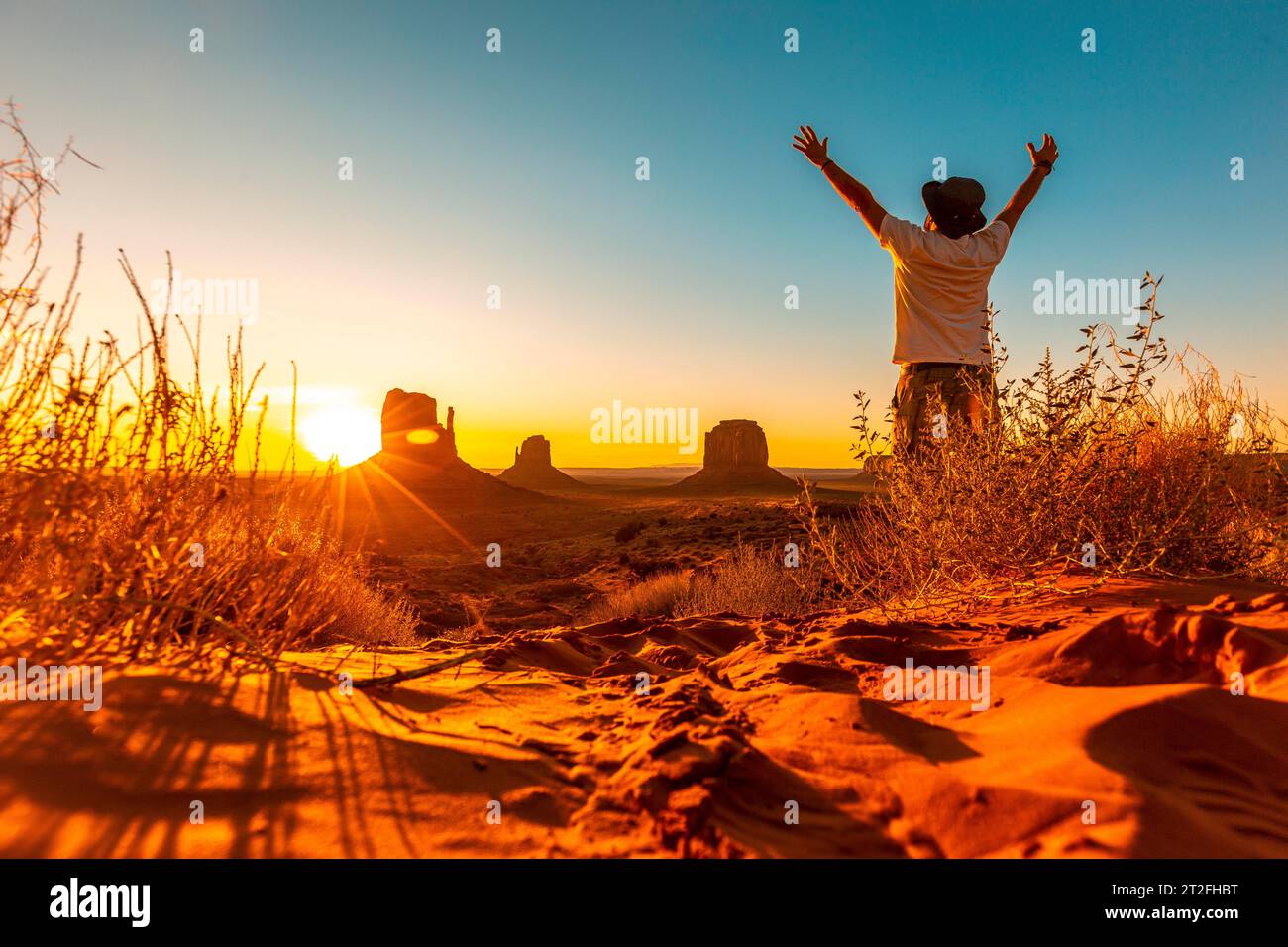 Ein Lifestyle-Typ mit Hut und offenen Armen bei Sonnenaufgang in Monument Valley, Utah Stockfoto