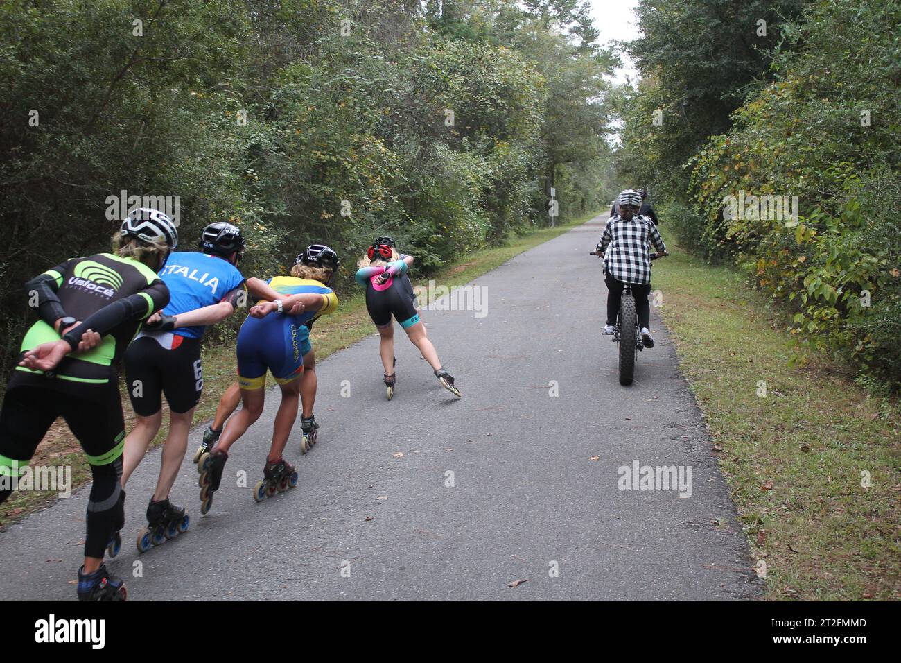 Inlineskater, die eine Familie von Radfahrern passieren (Gruppenaktivitäten auf einem Pfad) Stockfoto