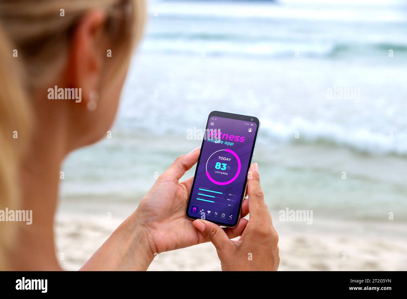 Workout mit der Online-Übungs-App auf dem Telefon. Frau am Strand mit digitalem Personal Trainer mit Smartphone beobachten. Internet-Bus. Sportroutinen Stockfoto