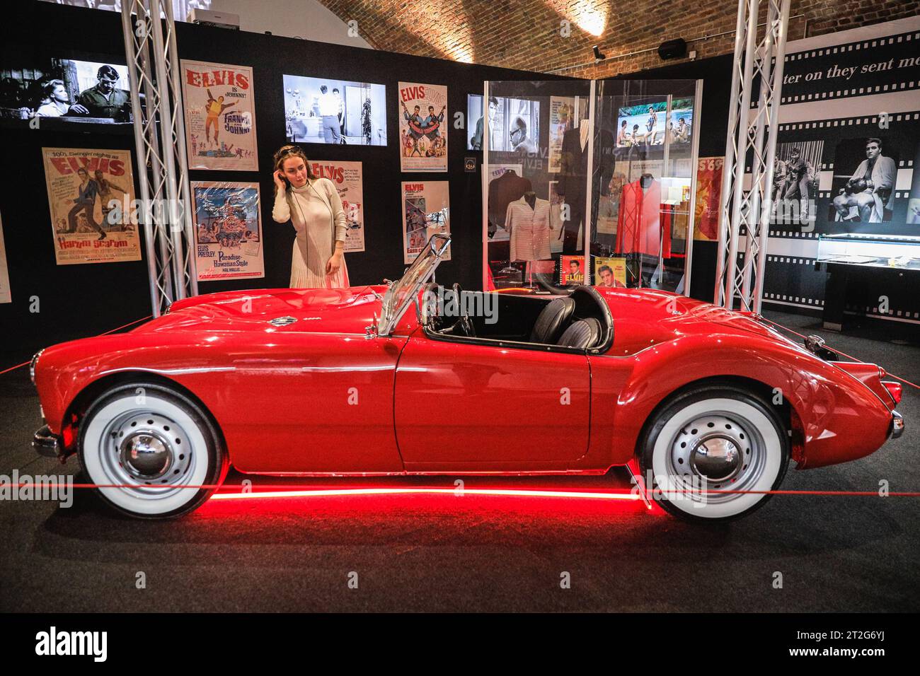 London, Großbritannien. Oktober 2023. Ein Besucher posiert mit Elvis' 1960 MGA 1600 MKI, dem einzigen von Elvis' persönlichen Autos, das in einem seiner Filme endete, der 1961 in dem Film Blue Hawaii verwendet wurde. Die Ausstellung „Direct From Graceland: Elvis“ zeigt über 400 Artefakte und ikonische Gegenstände, die Elvis gehört, direkt aus dem Haus des Ikons in Graceland in Memphis, Tennessee. Die Ausstellung wird am 20. Oktober in der Arches London Bridge in der Bermondsey Street eröffnet. Quelle: Imageplotter/Alamy Live News Stockfoto