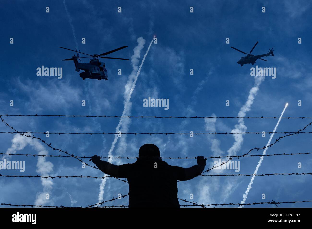 Person am Stacheldrahtzaun mit Beschuss und Hubschraubern im Hintergrund. Flüchtling, Krieg, Konflikt, Israel, Gaza, Palästina... Zusammengesetztes Bild des Konzepts. Stockfoto