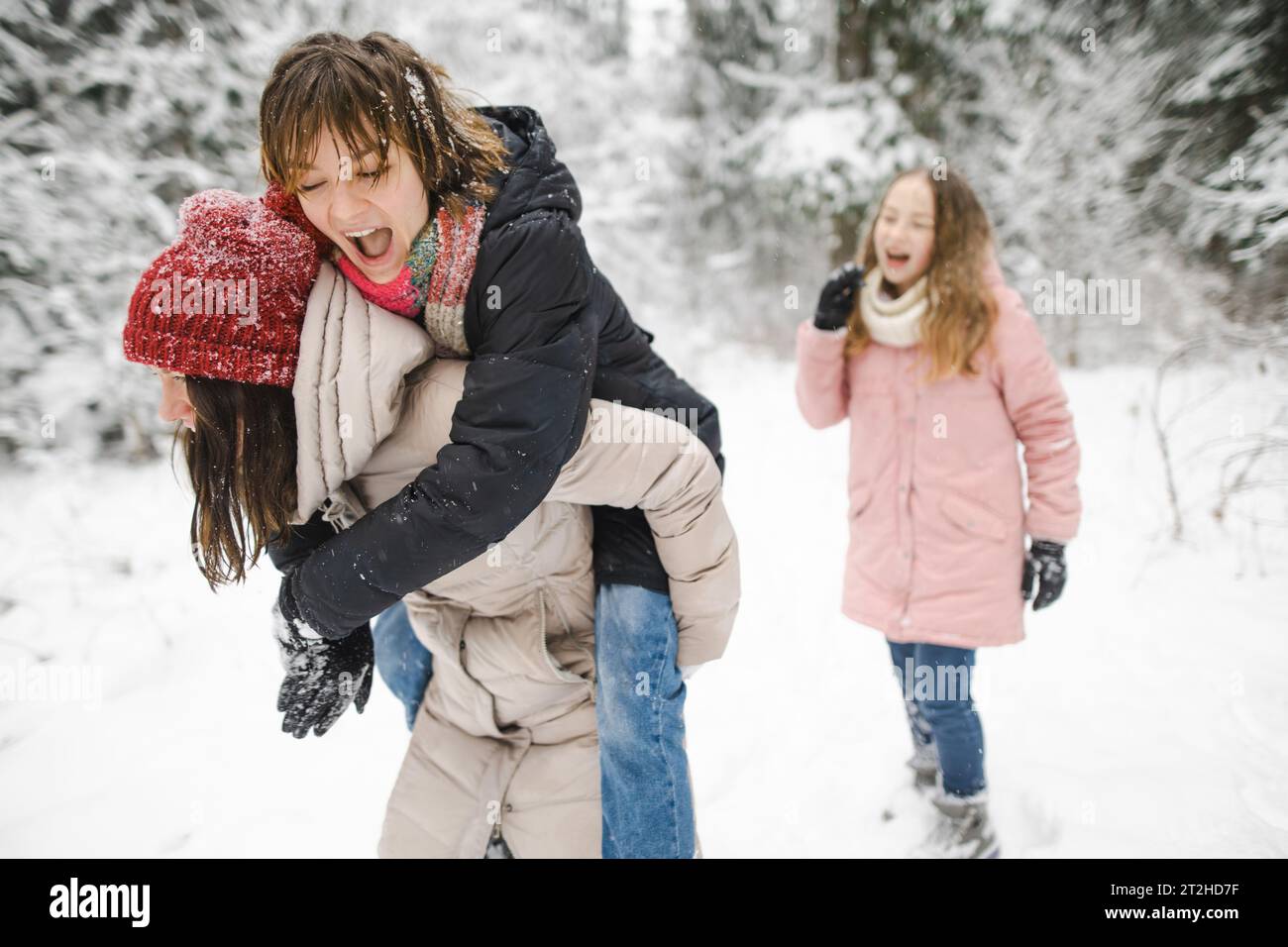 Lustige Teenager-Schwestern und ihre Mutter haben Spaß bei einem Spaziergang durch schneebedeckten Kiefernwald an einem kalten Wintertag. Teenager-Mädchen erkunden die Natur. Winter-Akti Stockfoto