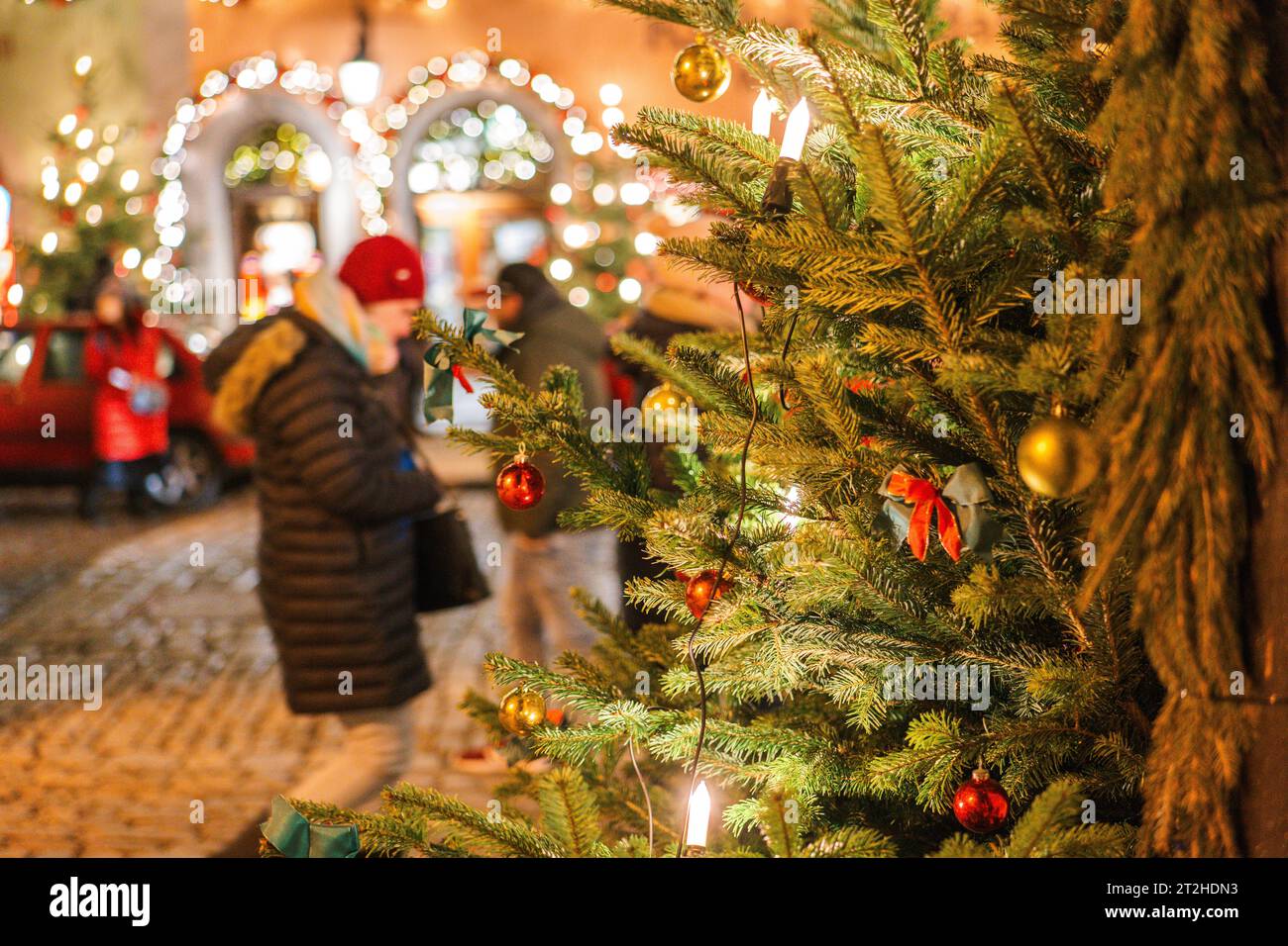 Weihnachtliche Stadt im Hintergrund. Leuchtende Läden und Weihnachtsdekorationen auf den Straßen Deutschlands. Weihnachtsbaum mit Girlanden und Menschen, die draußen sind Stockfoto