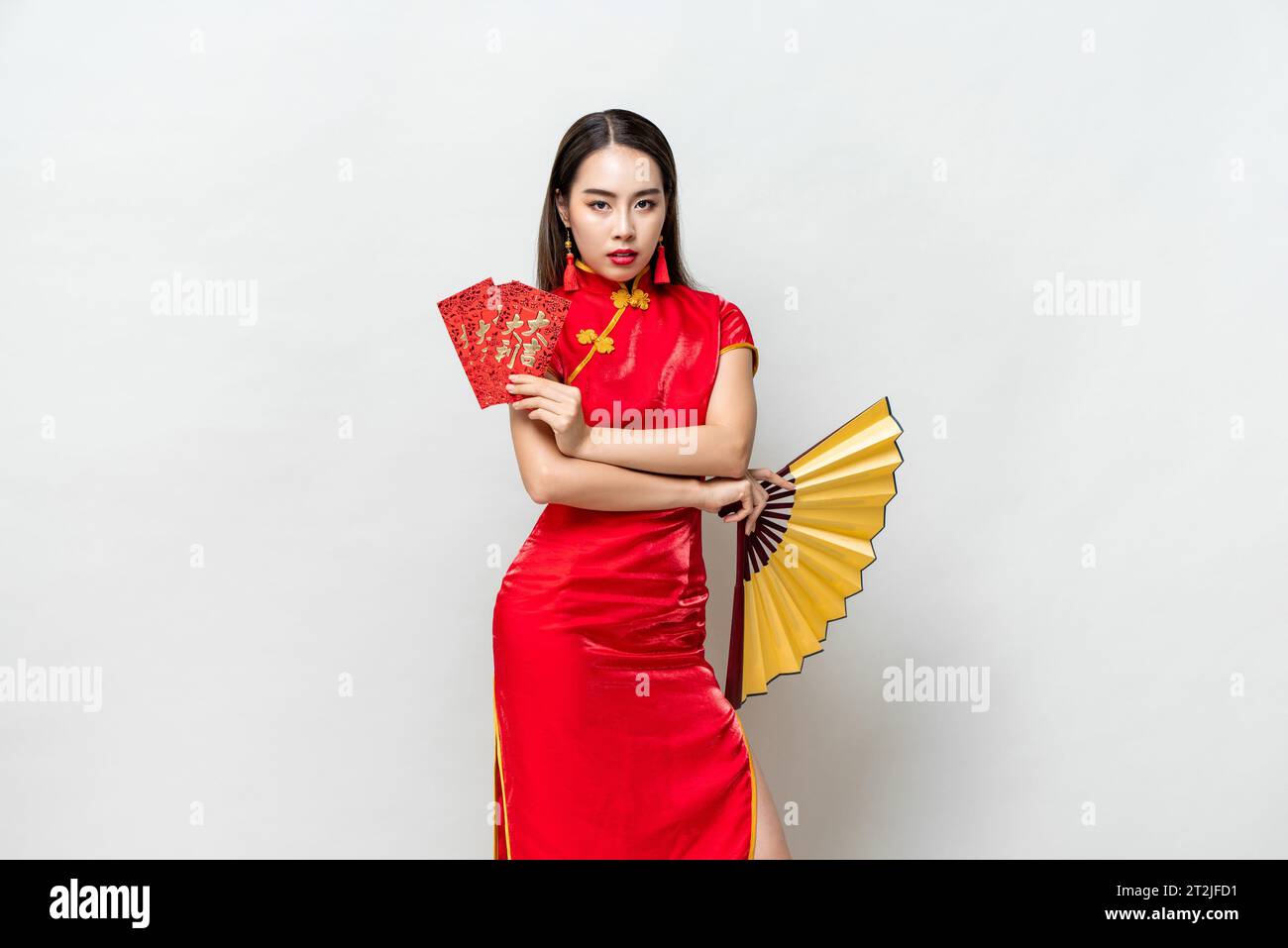 Asiatische Frau im orientalischen Cheongsam Kostüm, die rote Umschläge hält Ang Pow und Fan posiert auf hellgrauem Studiohintergrund für chinesische Neujahrskonzepte, Stockfoto