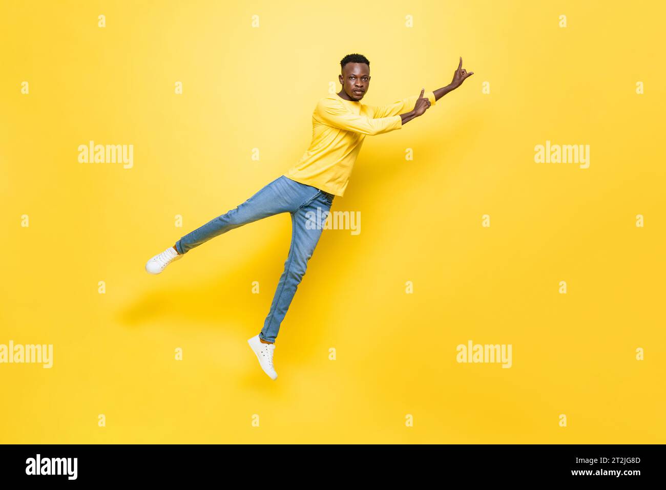 Ganzer Körper eines afrikanischen Mannes in Freizeitkleidung, der im Studio auf isoliertem gelbem Hintergrund schweben und die Hände nach oben zeigt Stockfoto
