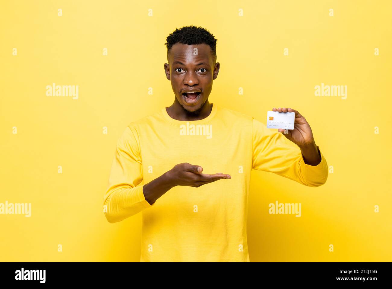 Schockierter afrikanischer Mann in lässiger Kleidung mit Kreditkarte auf gelbem Studiohintergrund Stockfoto