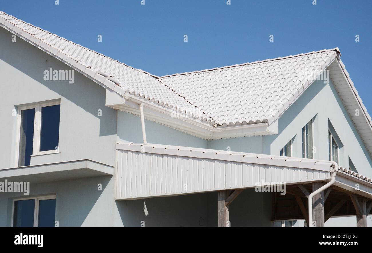 Weiß gekacheltes Dachhaus mit Regenrinnen-Pipeline, Soffits und Abdichtung im Problembereich. Dachkonstruktion. Stockfoto