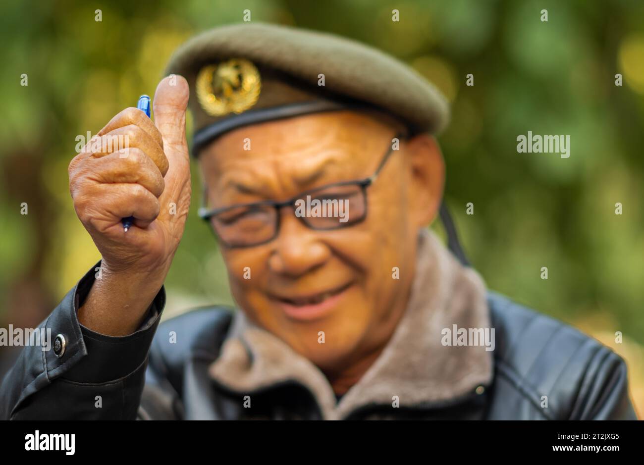 Ein älterer vietnamesischer Mann, der eine olivgrüne Baskenmütze und eine Lederjacke trägt, hält einen biro-Stift und gibt in Hanoi, Vietnam, die Daumen hoch. Stockfoto
