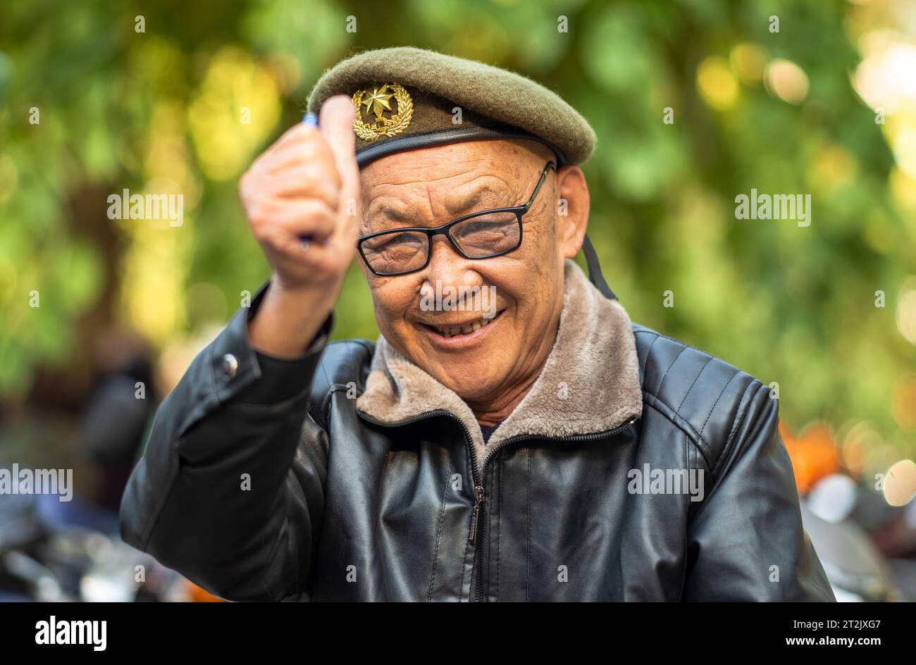 Ein älterer vietnamesischer Mann mit olivgrüner Baskenmütze und Lederjacke gibt in Hanoi, Vietnam, die Daumen hoch. Stockfoto