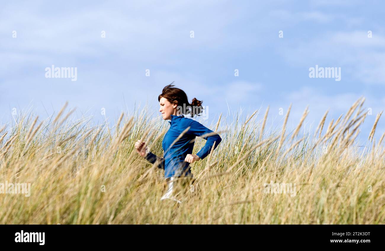 Eine Frau, die auf einem Sandweg mit hohem Gras am Meer läuft. Stockfoto