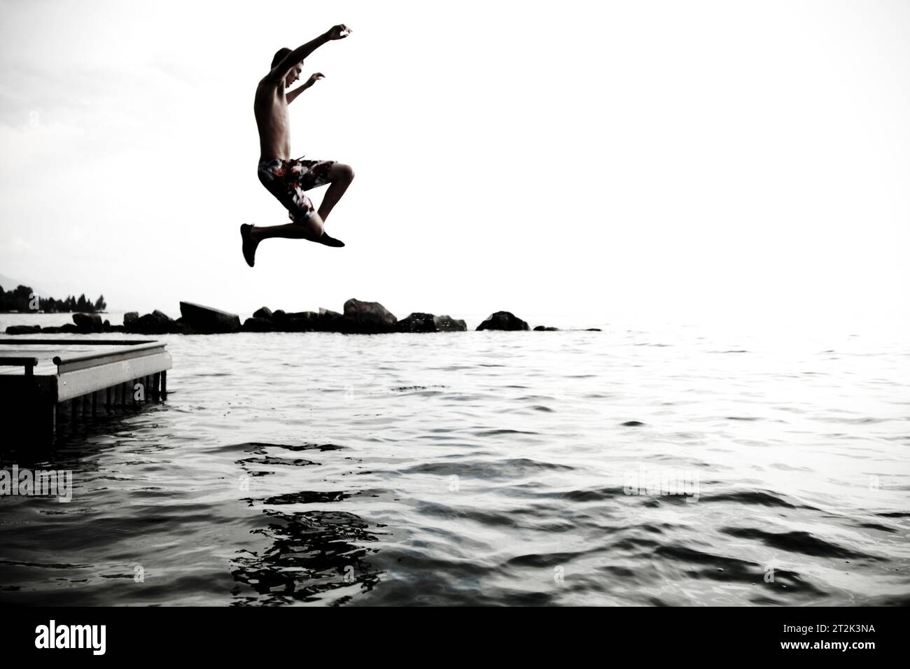 Ein junger Teenager wirft seine Arme in die Luft, während er von einem Dock springt, um im kühlen Wasser des Flathead Lake, Montana, zu schwimmen. Stockfoto
