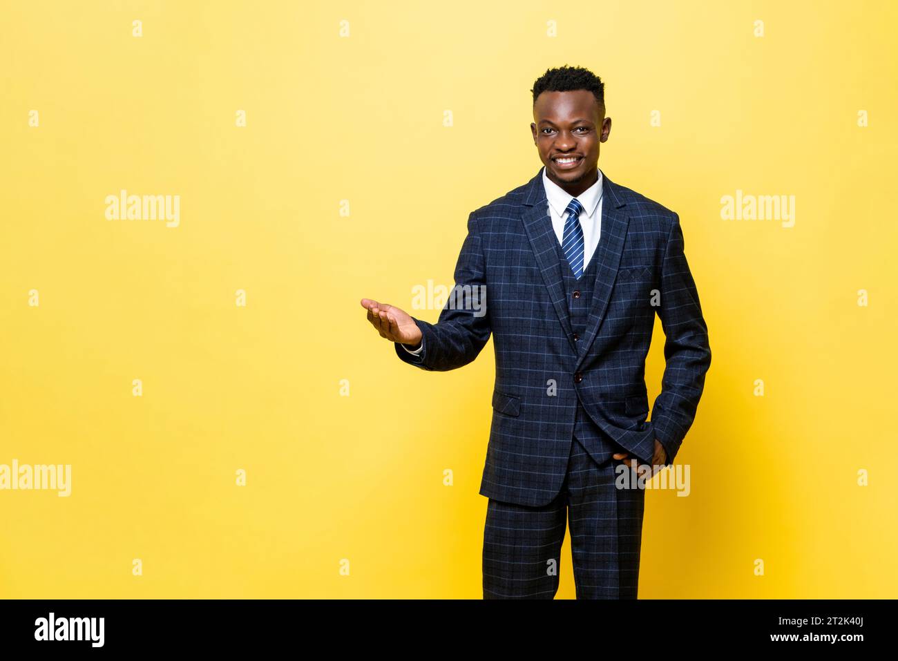 Positiver afrikanischer Mann im formellen Business-Anzug lächelnd und öffnende Hand, die Willkommensgeste in gelbem Farbstudio isolierten Hintergrund tut Stockfoto