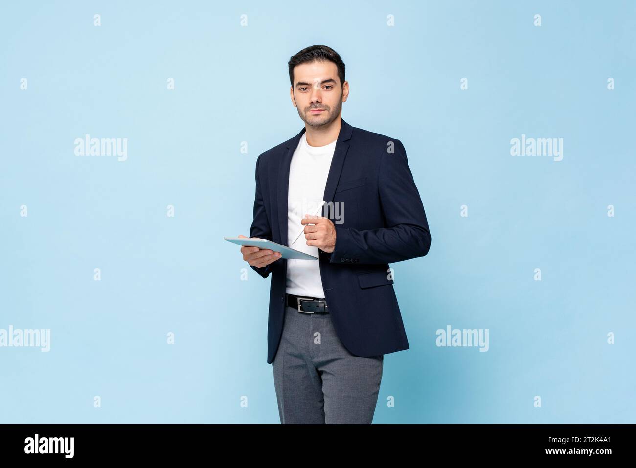 Intelligenter gutaussehender kaukasischer Mann im halbformalen Business-Anzug, der Tablet-Computer mit Stift in hellblauer Farbe isoliert Studiohintergrund hält Stockfoto