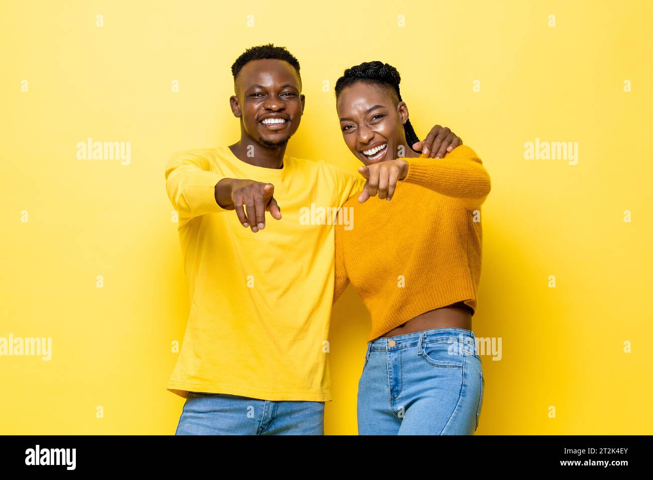 Glückliches afrikanisches Paar, das sich gegenseitig hält und mit den Händen auf dich zeigt, in gelbem Farbstudio isoliertem Hintergrund Stockfoto