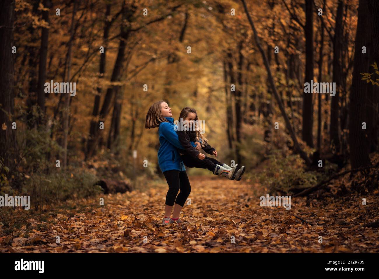 Schwestern drehen sich und spielen in bunten Herbstblättern Stockfoto