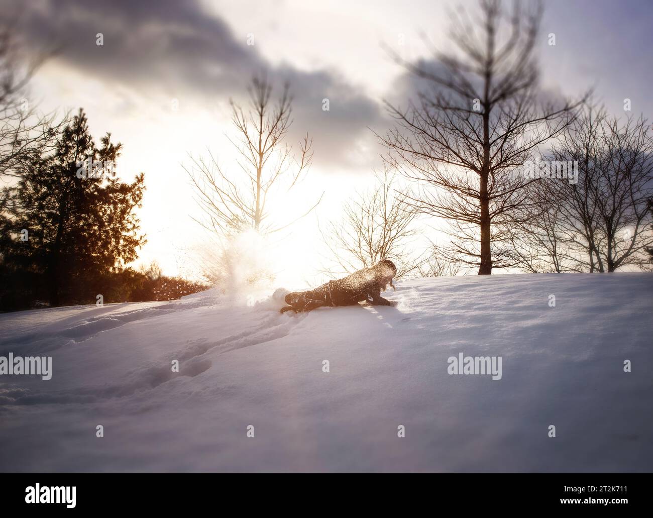 Kleines Kind, das im Winter den schneebedeckten Hügel hinunterfährt Stockfoto