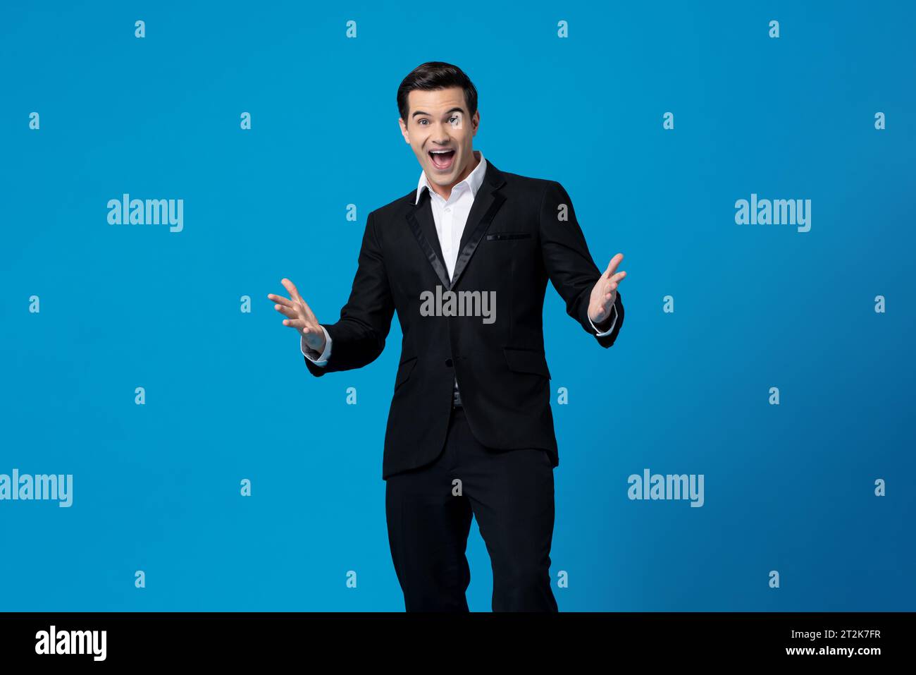 Porträt eines gutaussehenden, fröhlichen kaukasischen Millennial-Geschäftsmannes in schwarzem Anzug mit geöffneter Geste und Blick auf die Kamera über isoliertem blauem Hintergrund Stockfoto