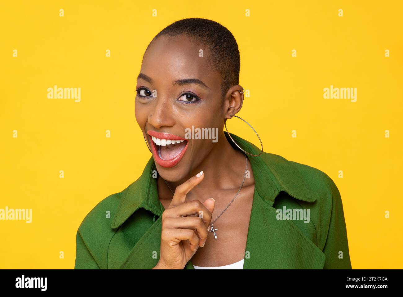 Nahaufnahme Porträt eines rasierten Kopfes afroamerikanischer stilvoller Frau mit offenem Mund, lachend und mit dem Finger über isoliertem gelbem Hintergrund Stockfoto