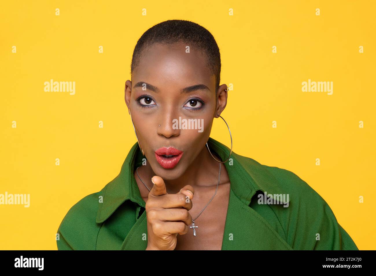 Nahaufnahme eines Porträts einer selbstbewussten afroamerikanischen jungen Frau mit rasiertem Kopf, der auf gelbem Hintergrund in die Kamera zeigt und kommandiert Stockfoto