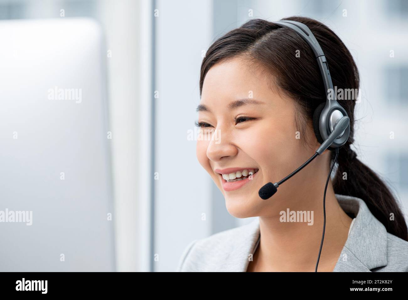 Lächelnde, schöne asiatische Kundendienstanbieterin, die ein Headset trägt und im Callcenter arbeitet Stockfoto