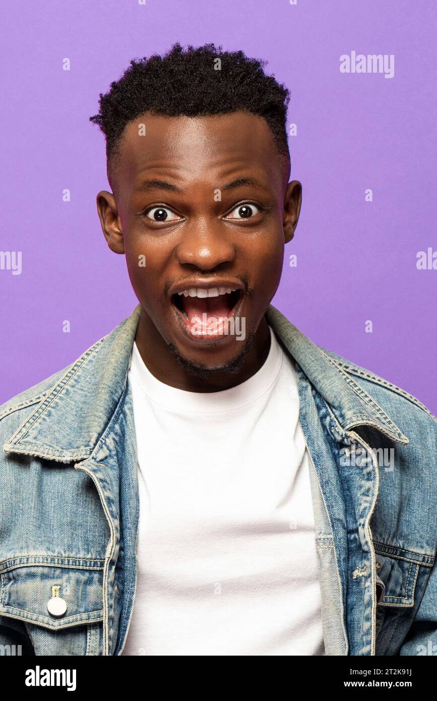 Junger afrikanischer Mann, der überraschtes Gesicht mit knallenden Augen in isoliertem lila Farb-Studio-Hintergrund ausdrückt Stockfoto