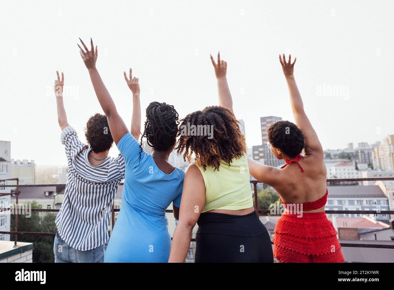 Vier Freunde winken mit den Händen und zeigen ein Friedenssymbol. Mann und afrikanische Frauen stehen mit dem Rücken und betrachten Stadtgebäude aus der Höhe. Mixe Stockfoto