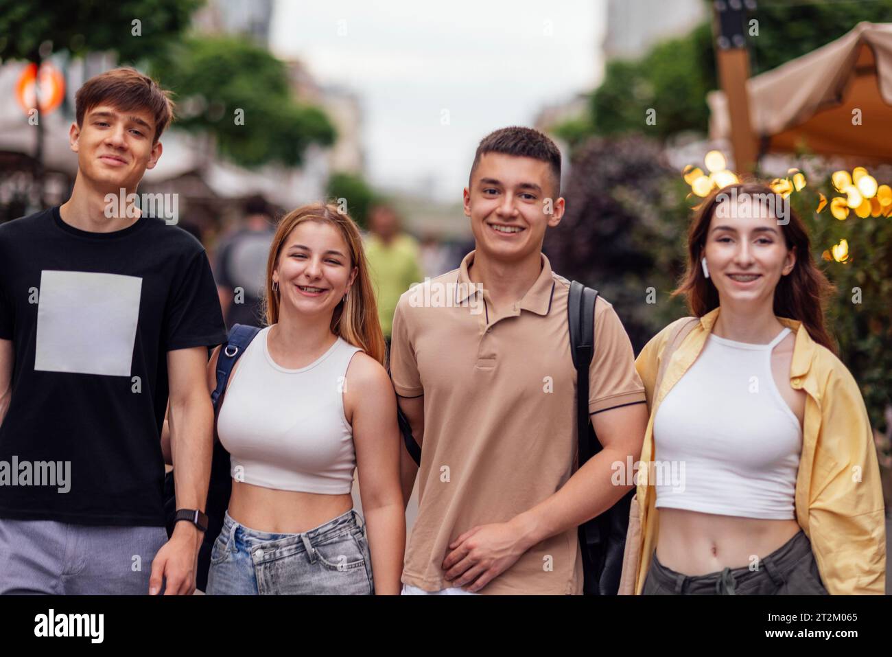 Vier Freunde in lässiger Kleidung laufen durch die Stadt. Teenager lachen und haben Spaß. Zwei Jungs und zwei Mädchen draußen auf der Straße. Fröhliche Teenager Stockfoto