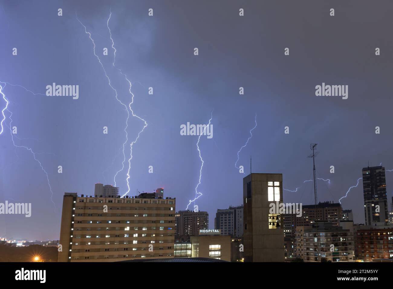 Stürmischer Himmel mit mehreren riesigen Blitzschlägen, die am Rande einer Stadt über Gebäuden auf den Boden schlagen. Wetterkonzept Stockfoto