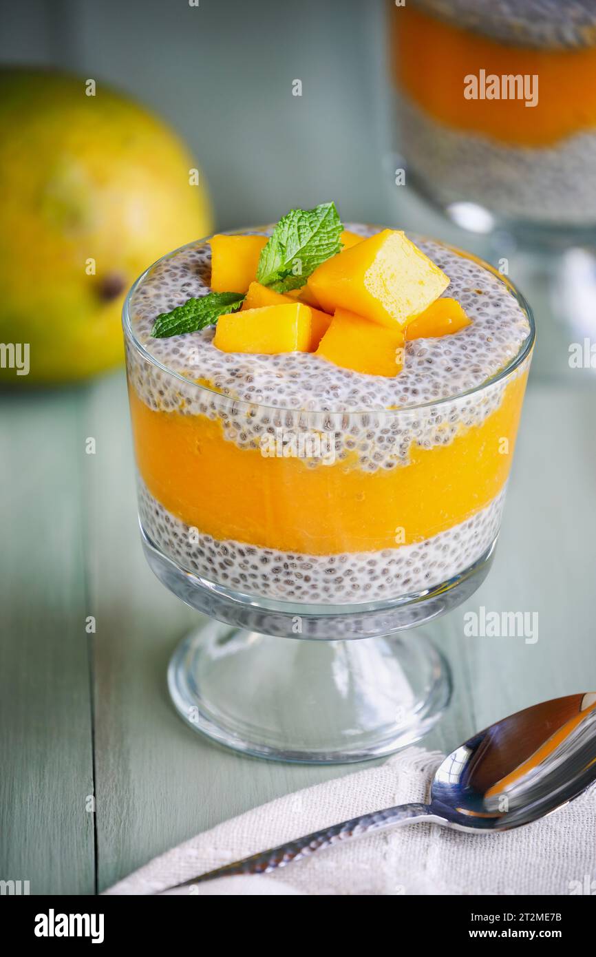 Köstlicher veganer Mango-Chia-Pudding mit frischen Minzquellen in einem Glas auf grünem Holzhintergrund. Selektiver Fokus mit unscharfem Hintergrund. Stockfoto