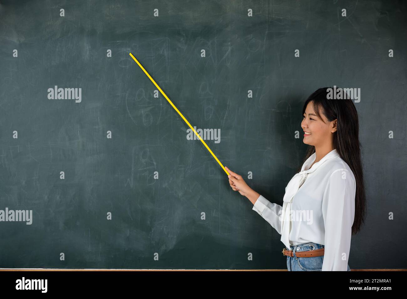 Asiatische Lehrerin lächelt mit Holzstab, der auf die Tafel zeigt Stockfoto