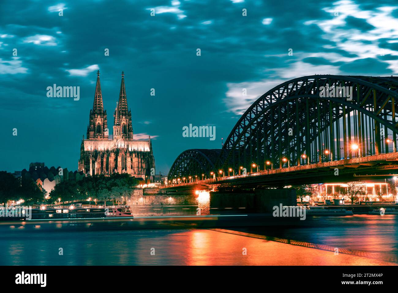 Kölner Dom und Hohenzollernbrücke am Abend mit künstlicher Beleuchtung gegen bewölkten Himmel Stockfoto