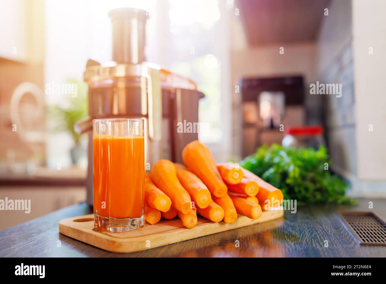 Ein Glas frisch gepressten Karottensaft, Karotten und Saftpresse in der Küche Stockfoto