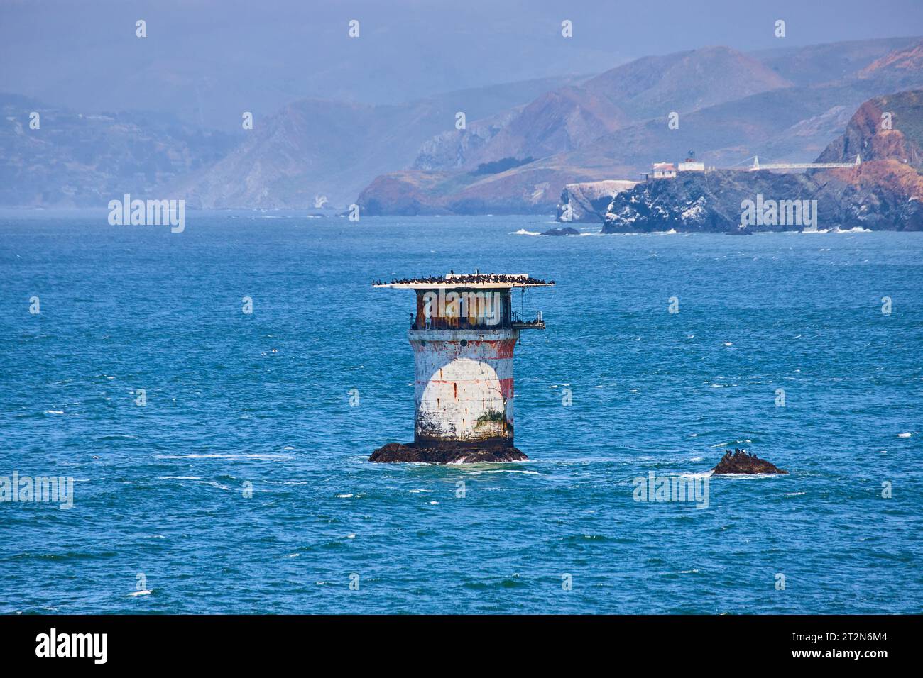 Verlassenes Leuchtturmgebäude in der Mitte der Bucht mit fernen bergigen Küsten Stockfoto
