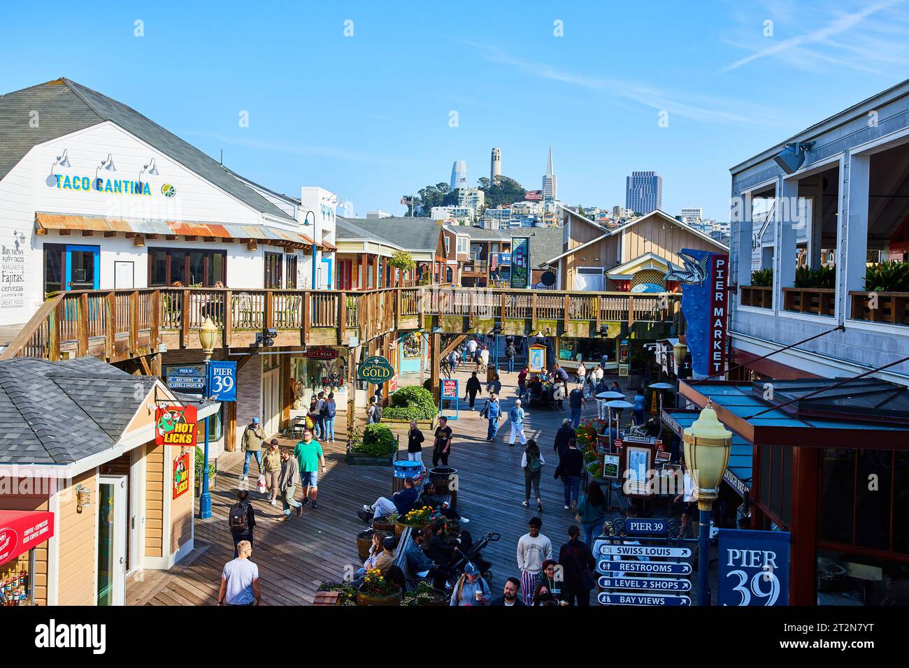 Leute laufen zu Fuß von Geschäften und Restaurants am Pier 39 mit Coit Tower in der Nähe Stockfoto