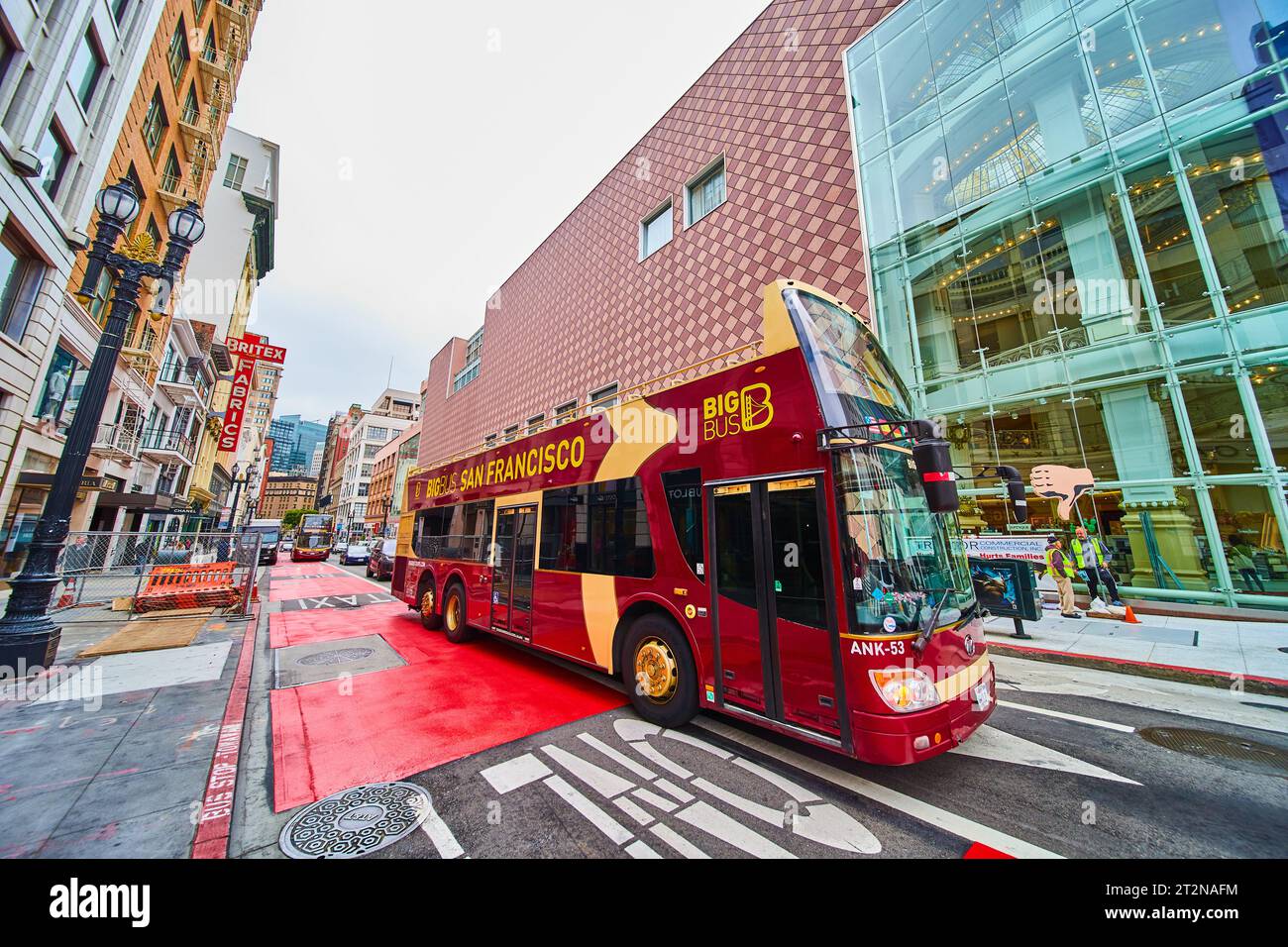 Großer Bus mit dunkelroter und gelber Färbung, der an einem langen Gebäude in San Francisco vorbeifährt Stockfoto