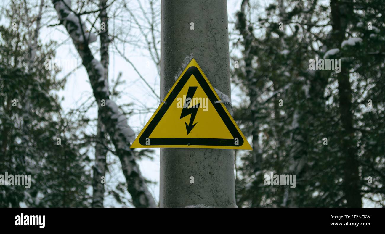 Gelbes Hochspannungsschild an einem Pol im Wald Stockfoto
