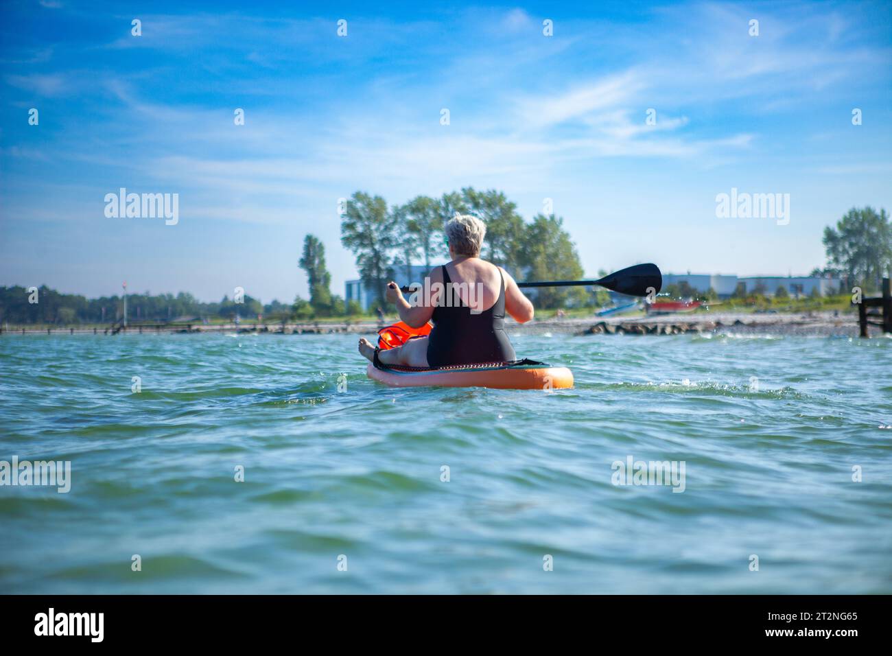 Eine mittelgroße Frau im Meer, die auf einem Paddelbrett sitzt Stockfoto