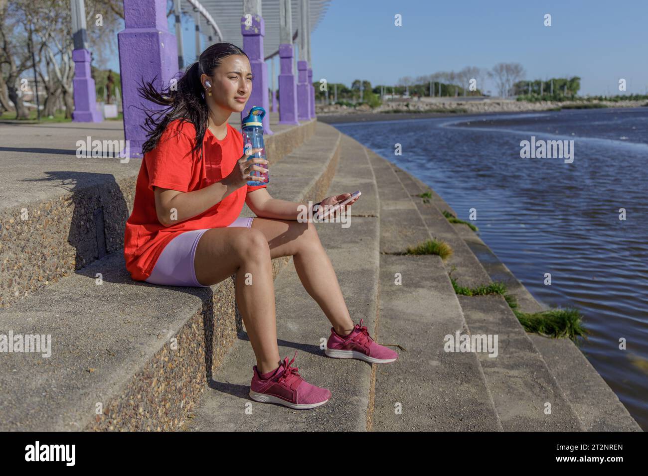 Mädchen in Sportbekleidung sitzt auf der Treppe und trinkt aus einer Flasche Wasser. Stockfoto