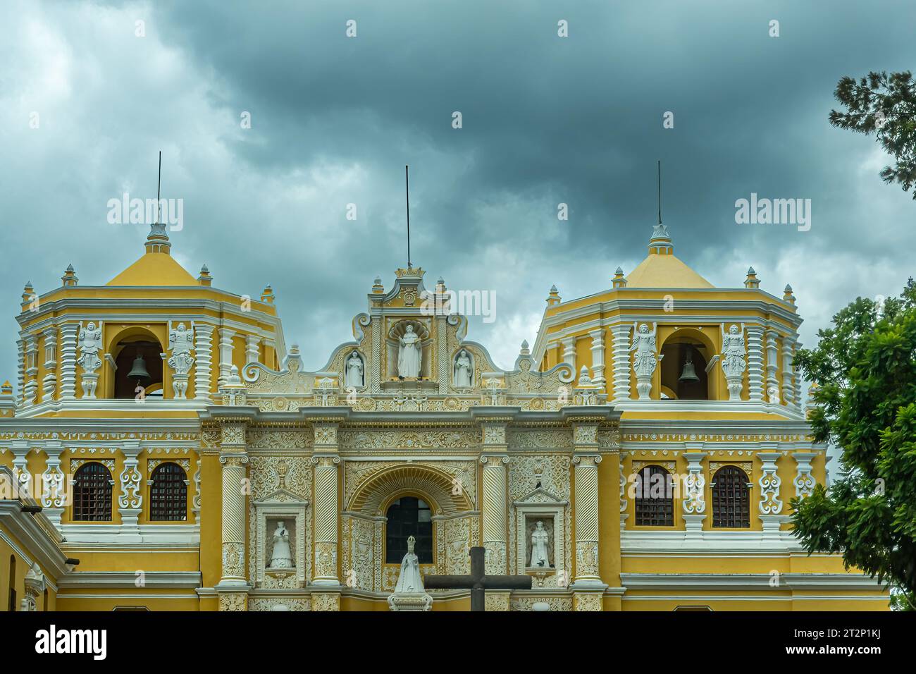 Guatemala, La Antigua - 20. Juli 2023: Klosterkirche Nuestra Senora de la Merced. Obere Ebene mit gelben Glockentürmen und Fassade, weiße Statuen in ni Stockfoto