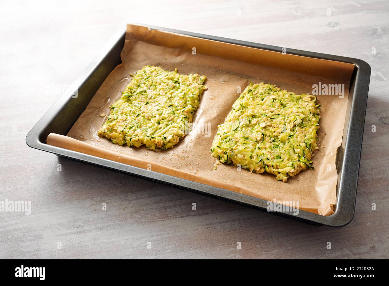 Teig Zucchini und Haferflocken als Basis für vegane Low Carb Pizza oder Gemüsekuchen auf einem Tablett mit Backpapier, Kopierraum, ausgewähltem Fokus, schmal d Stockfoto