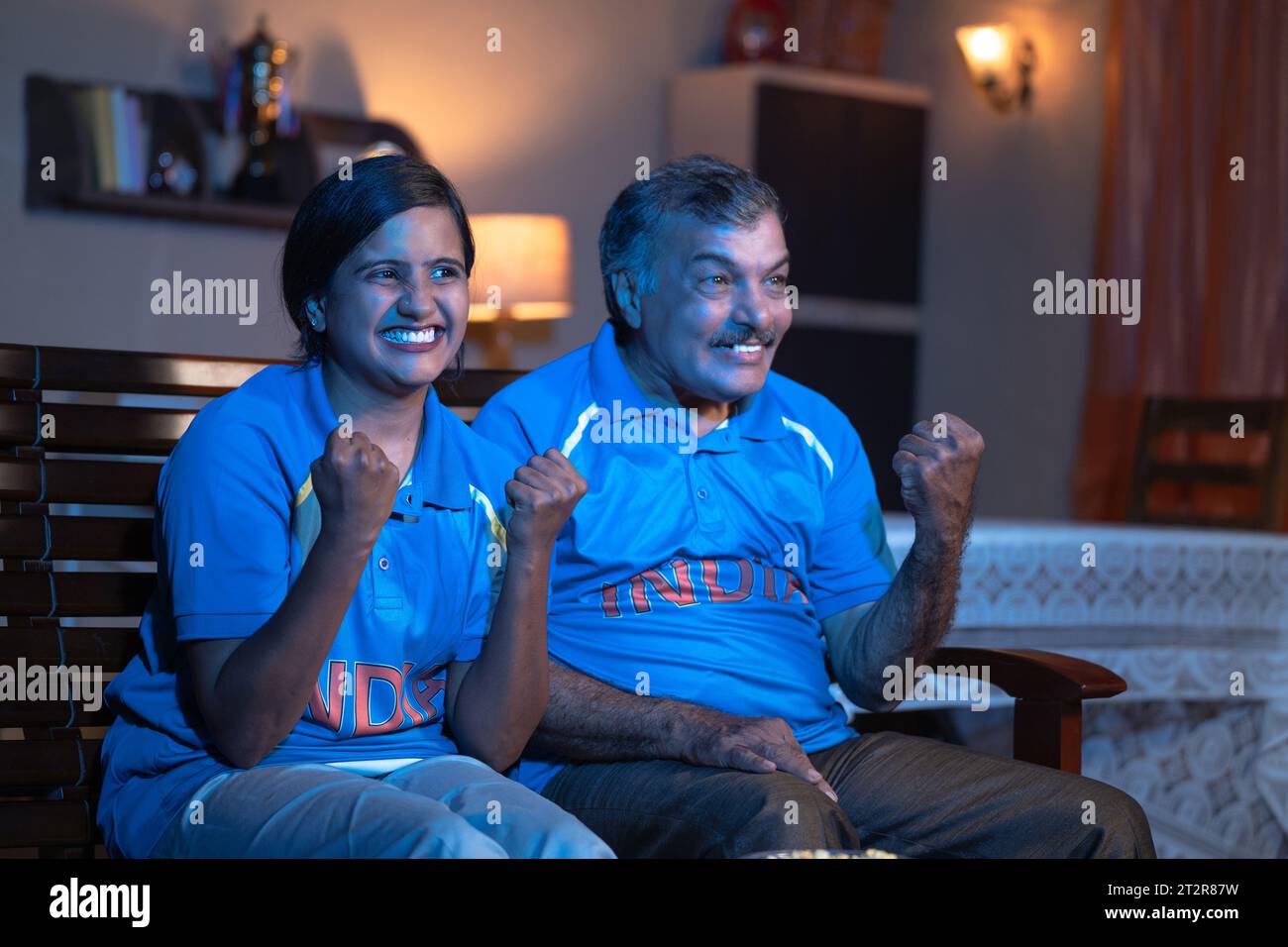 Seitenansicht des aufgeregten indischen Vaters und der Tochter, die als Indien schreien, während sie Cricket im fernsehen oder im Fernsehen zu Hause anschauen - Konzept des fröhlichen Feierns Stockfoto