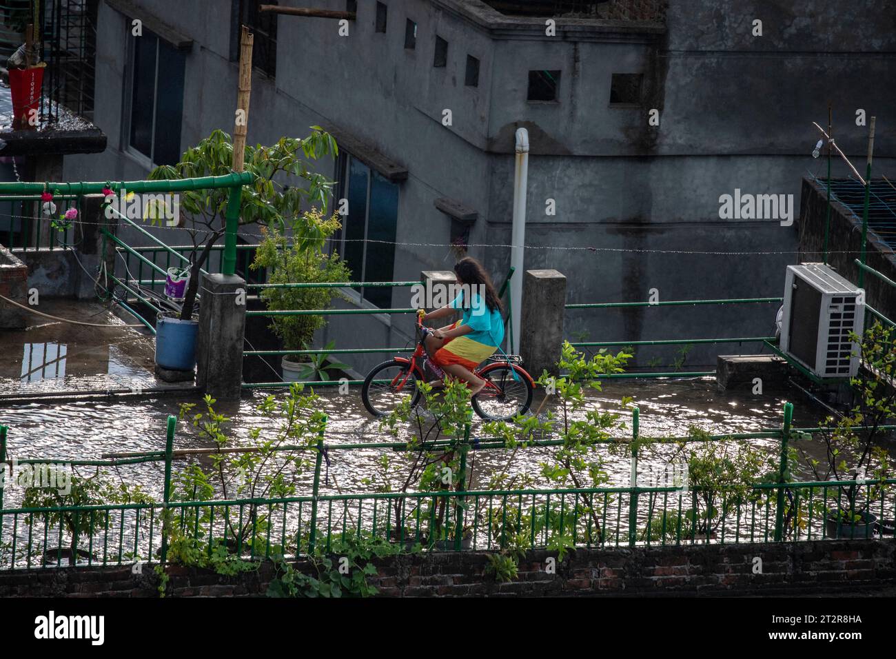 Ein Mädchen radelt mit dem Fahrrad über ein wasserdichtes Dach nach starken Regenfällen in Dhaka, Bangladesch Stockfoto