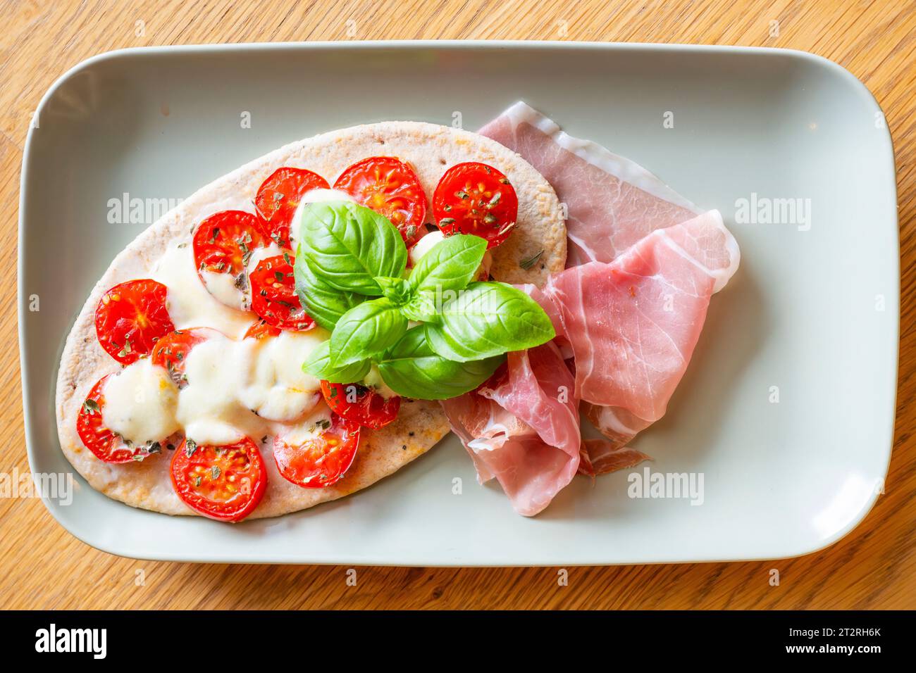 Tomaten-Mozzarella-Pita auf Fladenbrot mit frischem Parmaschinken und Basilikumblättern, serviert auf einem rechteckigen Teller Stockfoto