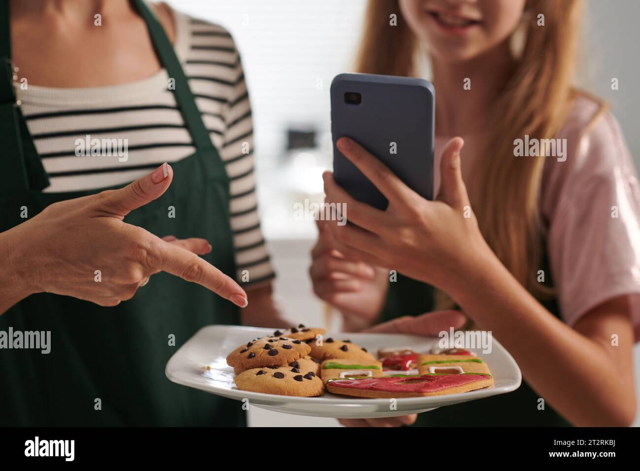 Mädchen fotografiert Teller mit Keksen, die sie und ihre Mutter gebacken haben, um Beiträge in sozialen Medien zu teilen Stockfoto
