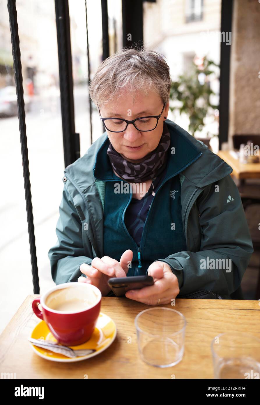 Ältere Frau, Best Ager, sitzt im Café, trinkt Kaffee, tippt Smartphone, Mobiltelefon, Paris, Frankreich Stockfoto