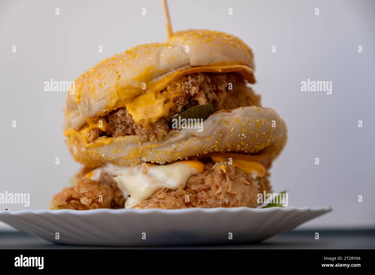 Chicken Burger mit Gurken, Brot, Sesam und Käse überall isoliert auf weißem Hintergrund mit Schüssel Stockfoto
