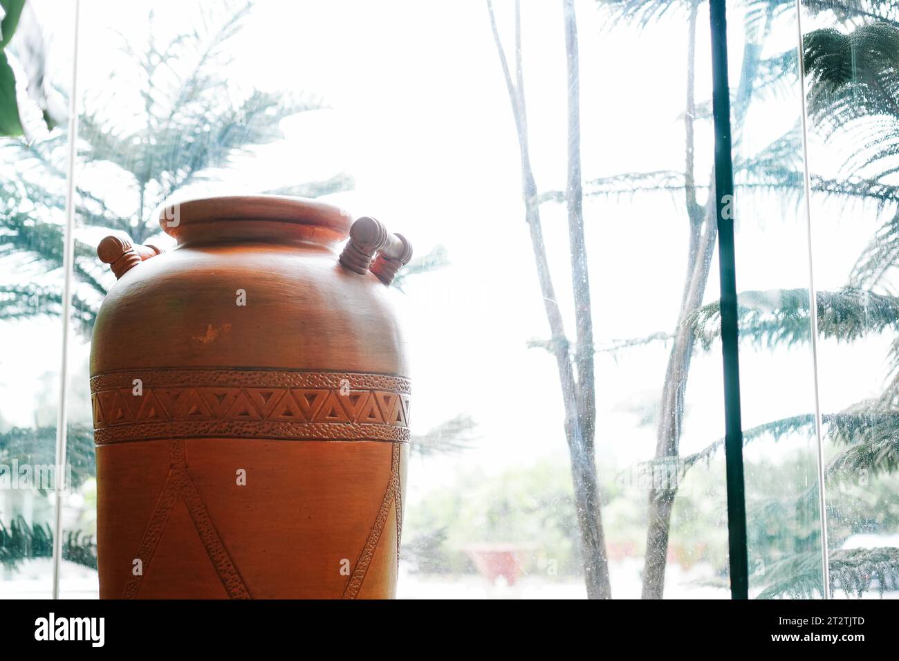 Wunderschön gefertigter brauner Krug mit kunstvollen Schnitzereien in der Nähe eines Glasfensters Stockfoto
