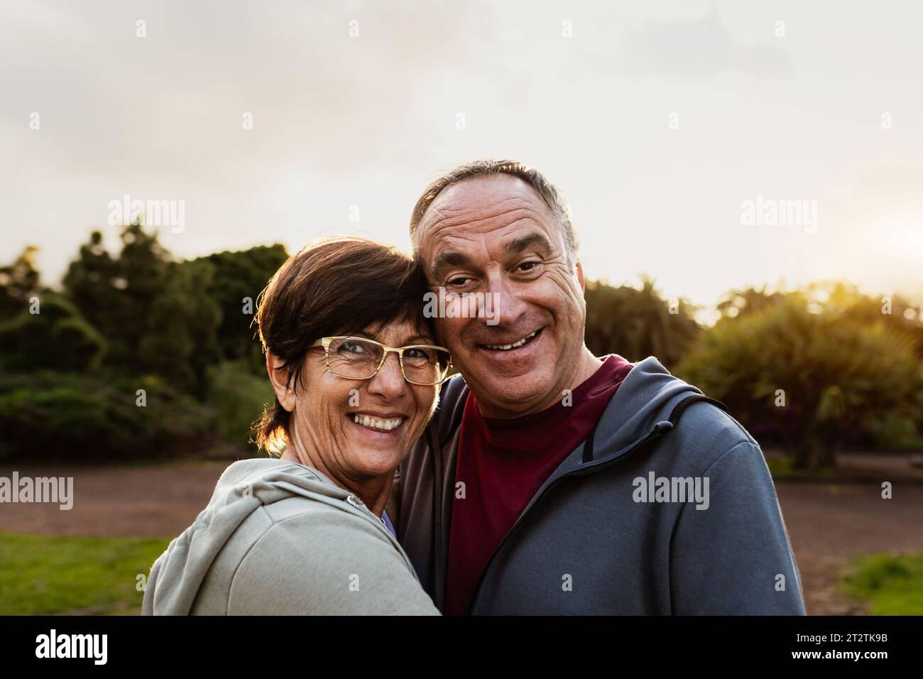 Glückliches Seniorenpaar, das Spaß hat, in die Kamera zu lächeln, nachdem sie in einem öffentlichen Park trainieren Stockfoto