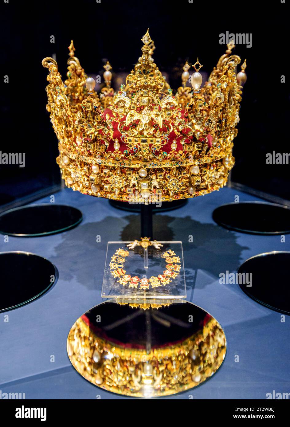 Goldene Krone mit Edelsteinen, die auf einem Miror reflektieren und isoliert auf schwarzem Hintergrund. Stockfoto